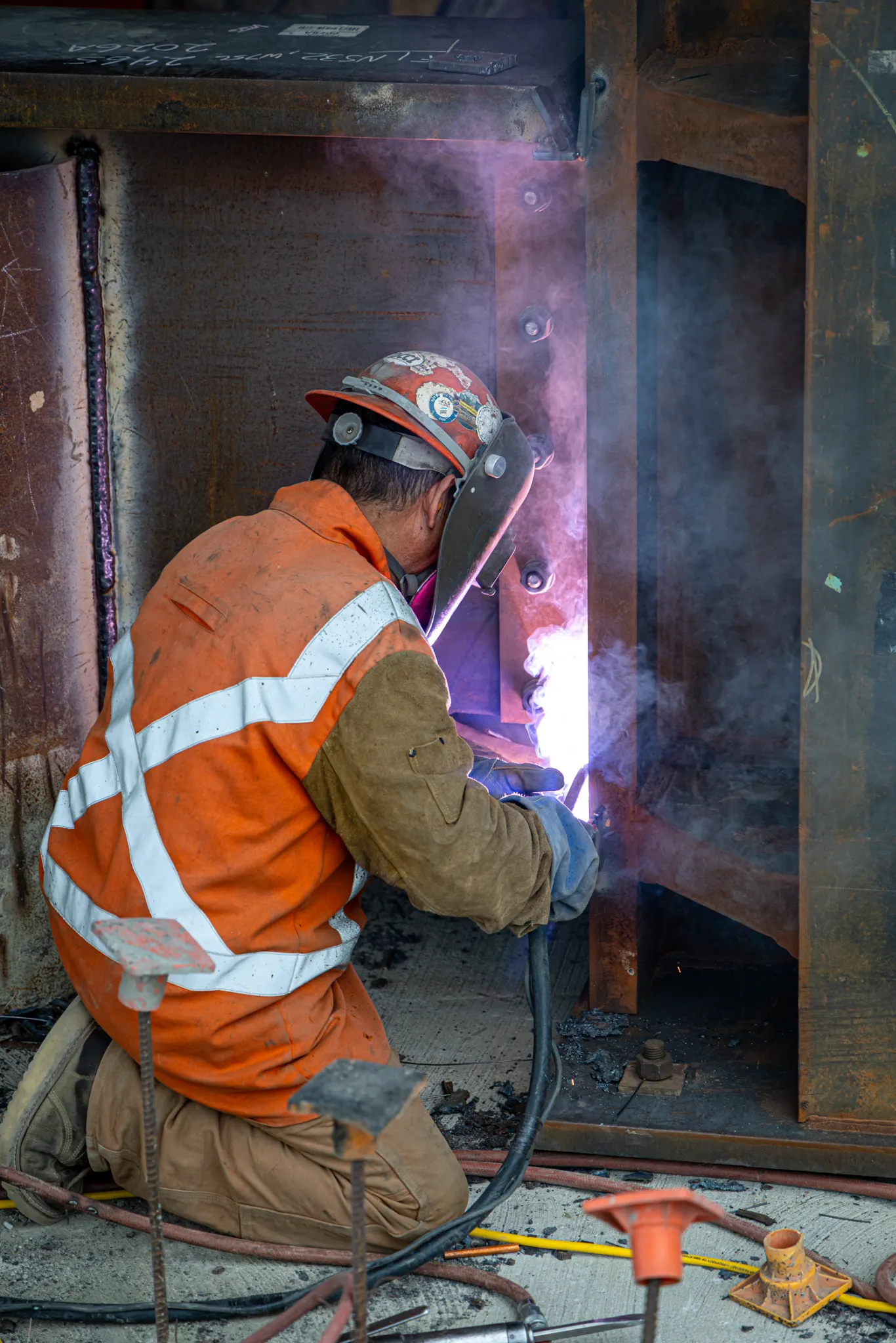 Welder in protective gear, kneeling down, welding a seam